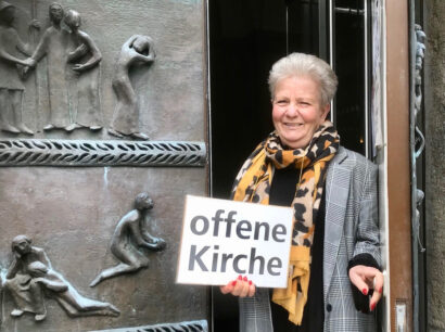 Anne de Wendt mit dem Schild "offene Kirche" im Eingangsportal der Reformationskirche